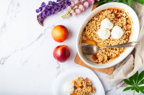 Preview: Fresh homemade nectarine crumble with vanilla ice cream in ceramic form on white marble background