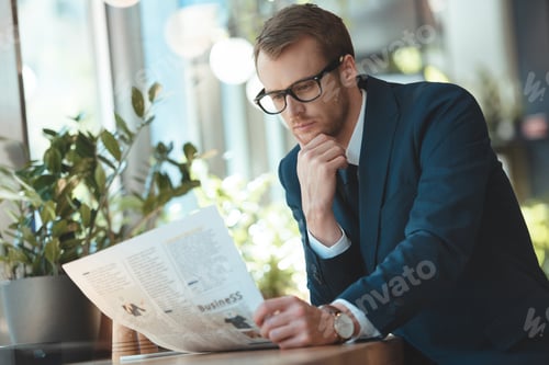 Preview: concentrated businessman in eyeglasses reading newspaper in cafe