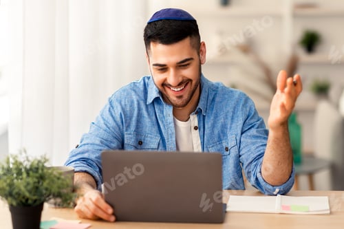 Preview: Smiling israeli man having videochat on laptop computer at home