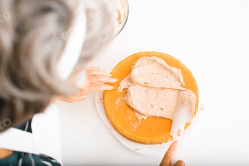 Preview: Close-up senior woman cook decorating cake with cream filling using spatula, housewife preparing