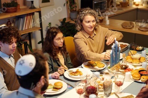 Preview: Smiling woman lighting menorah candles on candlestick before dinner