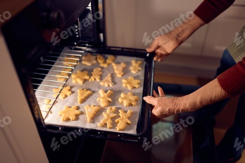 Preview: Close up of senior woman baking Christmas cookies in the oven.