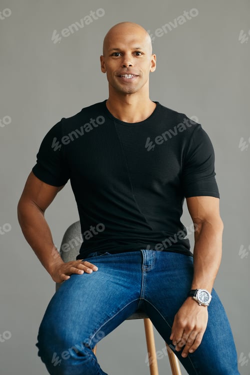 Preview: Portrait of handsome mixed race man sitting on a chair against gray background.