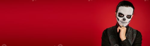 Preview: portrait of man in dia de los muertos sugar skull makeup holding hand near chin on red, banner