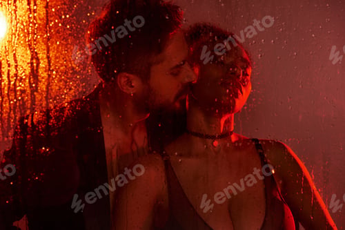 Preview: Intimate embrace of a passionate couple behind a rain streaked window at night