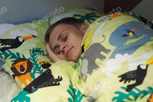 Preview: A young man sleeps in bed under a blanket.