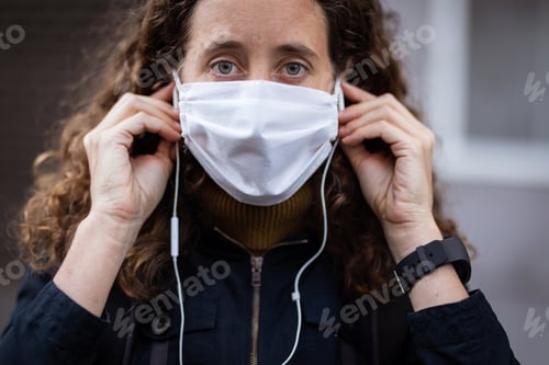 Preview: Caucasian woman putting on a protective mask in the streets and looking at the camera