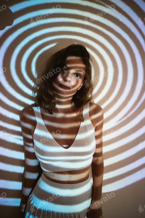 Preview: young adult woman or teenager girl in trendy outfit in dark room with projected geometrical illusion