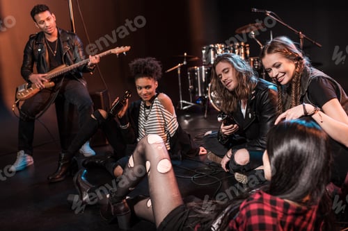 Preview: Young rock and roll band sitting together and drinking beer after concert on stage