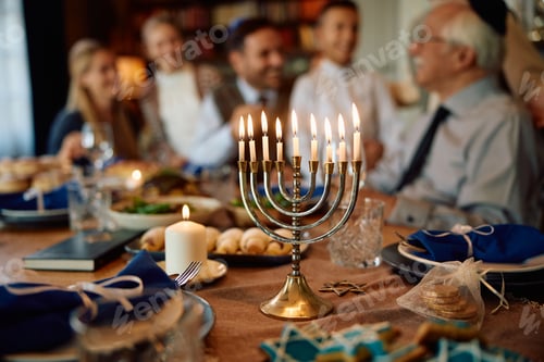 Preview: Lit candles in menorah with Jewish multigeneration family gathered for Hanukkah celebration.