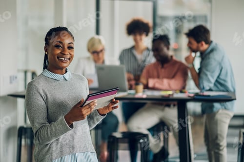 Preview: Black business woman standing in a office with colleagues in the back