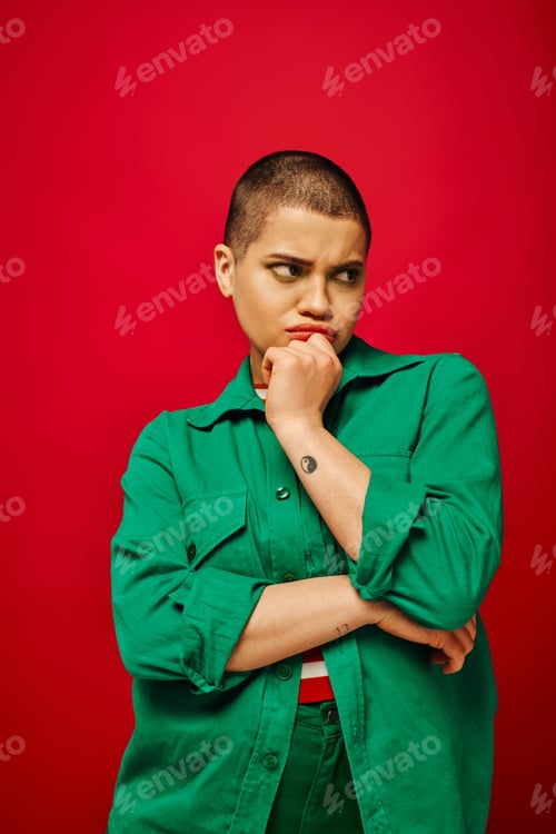 Preview: fashion choices, displeased and tattooed, short haired woman in green outfit touching chin on red