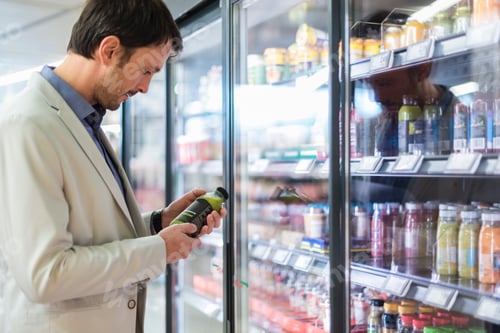 Preview: Mature man in supermarket choosing smoothie from cooling shelf