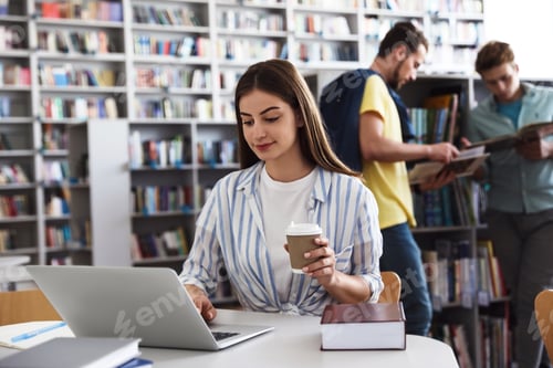Preview: Young woman studying at table in modern library