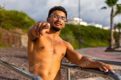 Preview: A fit young confident man with glasses and a beard indicates the camera with his hand