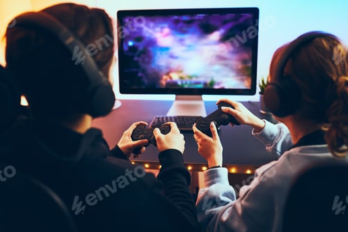 Preview: Friends playing video game at home. Gamers holding gamepads sitting at front of screen. Streamers