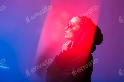 Preview: Portrait of fashion girl in a black sweater with a hood and sunglasses round shape in neon light in