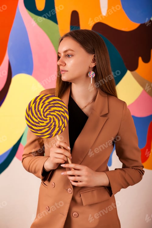 Preview: Pretty lady posing holding round giant lollipop at colored wall, pensive looking away