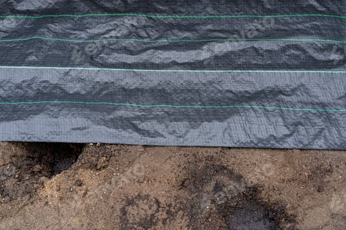 Preview: The plowed garden in front of the fence in the house, covered with black agrofiber.