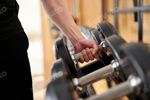 Preview: Hands of an Asian man taking dumbbells from a rack