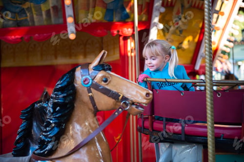 Preview: Cute little girl on the merry-go-round carousel in the amusement park.
