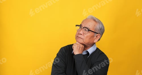 Preview: An old Asian man is thinking and deciding something. Isolated on yellow background in the studio.