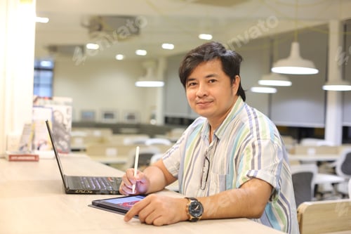 Preview: young Asian freelance designer smiling while look at camera against modern office.