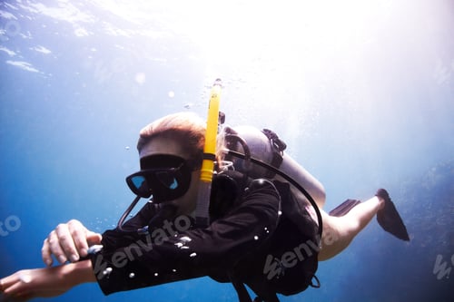 Preview: Young female scuba diver floating through the water as she checks her dive computer - Copyspace