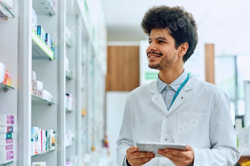 Preview: Happy Middle Eastern pharmacist using digital tablet while working in drugstore.