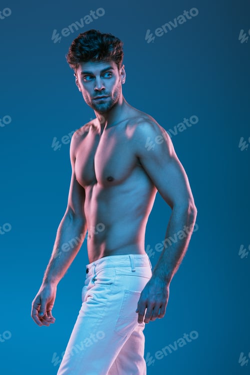 Preview: serious, sexy man in white jeans looking back while walking isolated on blue