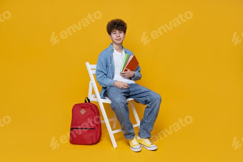 Preview: A happy teenager sits on a chair, on a yellow background