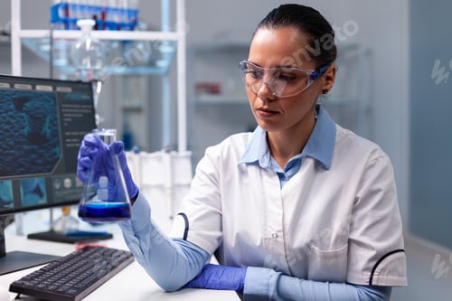 Preview: Chemist woman analyzing liquid solution holding medical glass flask
