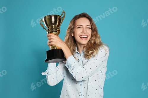 Preview: Portrait of happy young woman with gold trophy cup on blue background