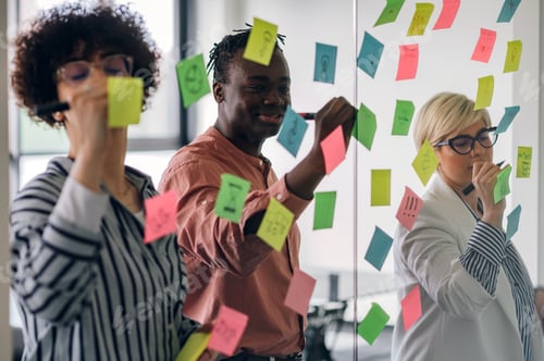 Preview: Multiracial team at work writing ideas on sticky notes on the glass wall