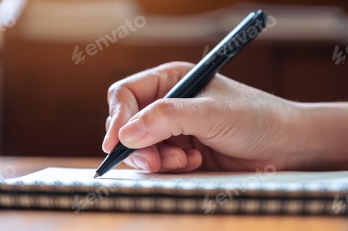 Preview: Closeup image of a hand writing down on a white blank notebook on wooden table