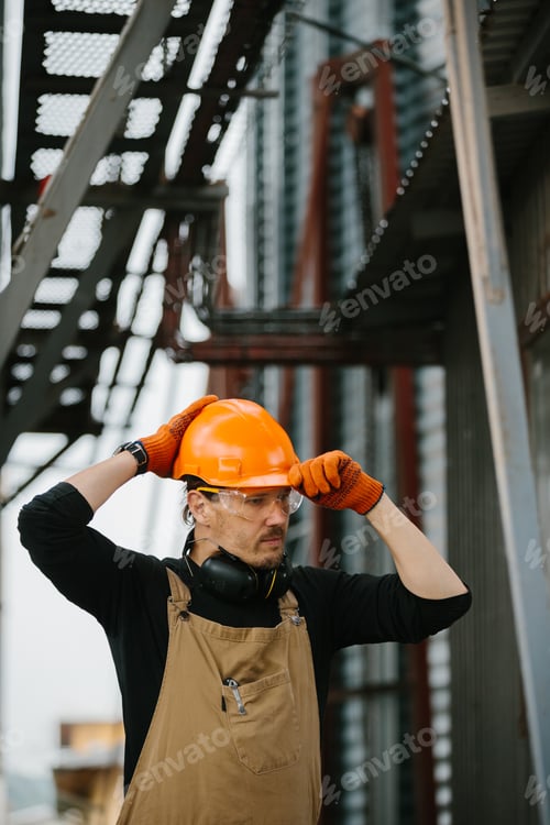 Preview: A worker adjusts his helmet. Builder installer at the construction site.