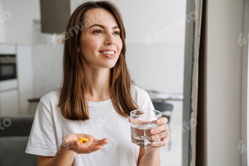 Preview: Smiling woman holding pills and glass of water