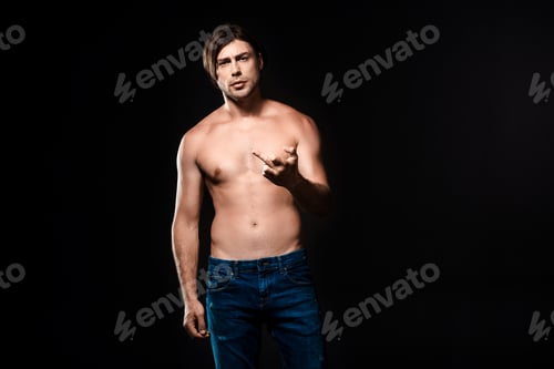Preview: portrait of shirtless man in jeans showing middle finger to camera isolated on black