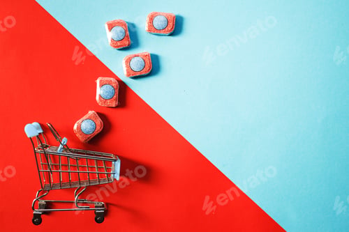 Preview: capsules for kitchen dishwashers and shopping cart on a blue and red background. flat lay.