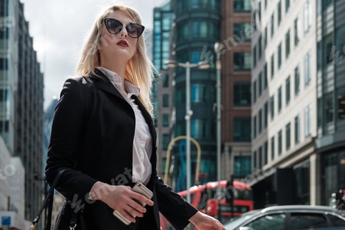 Visualização: Jovem empresária atraente usando óculos escuros e smartphones está parada na rua.