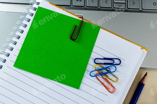 Preview: Top view of colorful paper clips on a blank notepad on a laptop