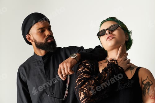 Preview: Stylish multicultural couple posing in trendy outfits with sunglasses in studio setting