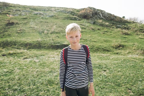 Preview: A blond boy 10 years old in a striped jacket with a red backpack goes on a hike in the fall.