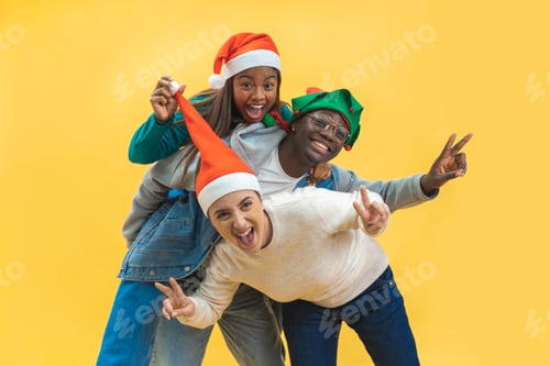 Vista previa: Happy three multiracial friends celebrating excited Christmas in yellow studio background.