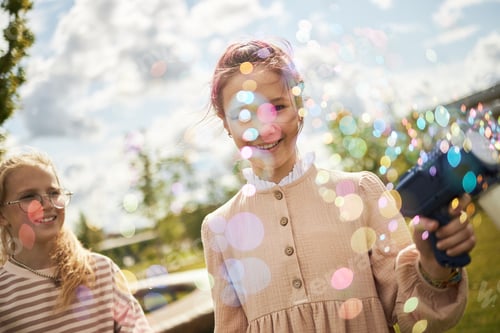 Preview: Caucasian Girls Smiling Outdoors While Blowing Bubbles in Sunlight