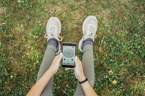 Preview: view from above of unrecognizable indian woman usinig running app sitting in park