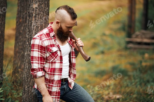 Preview: bearded lumberjack worker standing in forest with axe