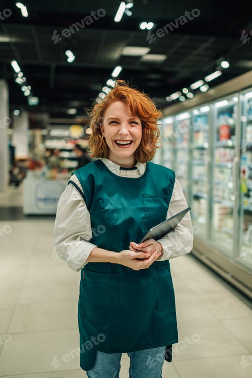 Preview: Smiling saleswoman holding digital tablet in supermarket aisle