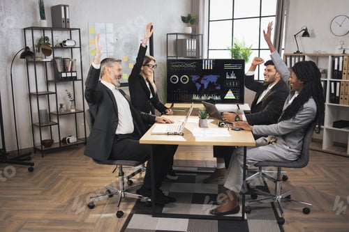 Preview: Smiling diverse multiracial businesspeople sit at office desk, celebrating successful project