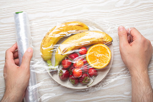 Preview: Male hands wrapping different fruit and berries on white plate in plastic clear film top view on